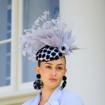 A V V Chapeaux Grey Squirrel button percher hat with Black lace daisy trim, Grey feather wisps, hand-cut spiky feathers and rolled ranunculus flowers.
